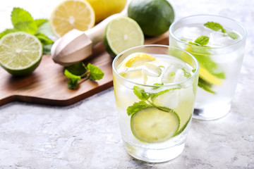 Two glasses of refreshing non alcoholic mojito lemonade drink with organic lemon, lime slices, mint leaves, straw, ice cubes on grunged grey concrete table background. Close up, top view, copy space.