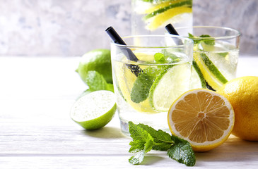 Vintage bottle with two glasses of refreshing non alcoholic mojito lemonade drink with lemon, lime slices, mint leaves, straw, ice on wooden table, concrete background. Close up, top view, copy space.