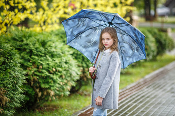 close up portrait of little beautiful stylish kid girl with an umbrella in the rain on park