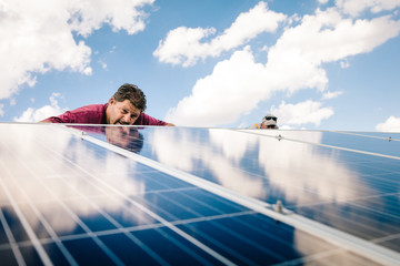Two workmen installing solar panels on roof of house, low angle view