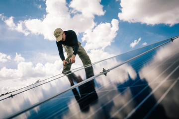 Workman installing solar panels on roof of house, low angle view