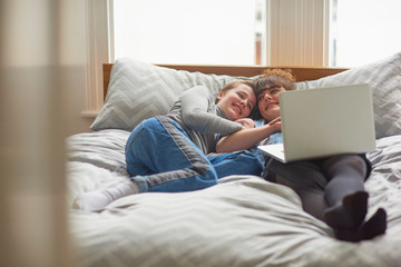 Friends using laptop on bed