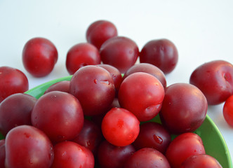 Ripe red plums in a green ceramic cup on a light background