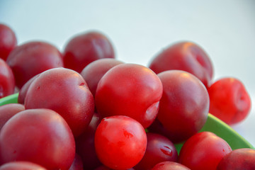 Ripe red plums in a green ceramic cup on a light background