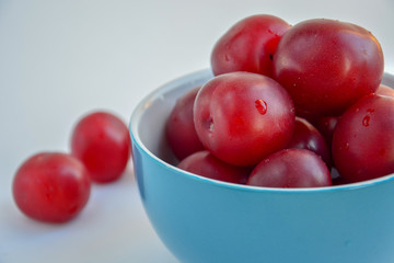Ripe red plums in a blue ceramic cup on a light background