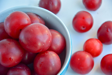 Ripe red plums in a blue ceramic cup on a light background
