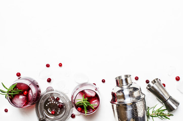 Cranberry cocktail with ice, rosemary and berries, bar tools, white background, top view
