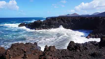 Los Hervideros rocky coast with wavy ocean and volcanos on the background, Lanzarote, Canary Islands, Spain                           