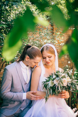 wedding day. Green garden and bench. Wedding photoshoot for newlyweds bride and groom. Kissing and huging couple.
