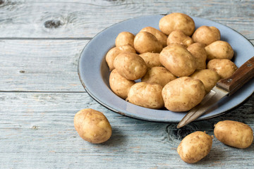 Young early potatoes in an old round bowl on a wooden table. 