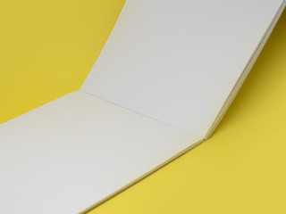 Vertically open blank notepad on a yellow background, close up