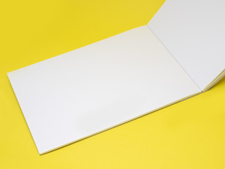Vertically open blank notepad on a yellow background, close up