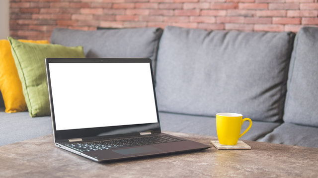 White Screen Laptop And A Yellow Cup On A Table By A Couch Mock Up