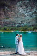 Attractive Young wedding couple standing on rocks next to river variation.  Bride and groom kiss each other behind the rock. Newlyweds photoshoot.