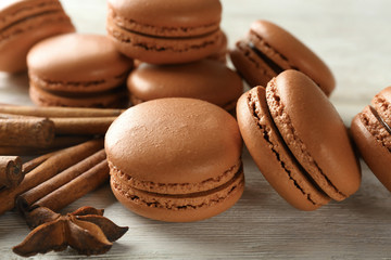 Tasty chocolate macarons and cinnamon on wooden background