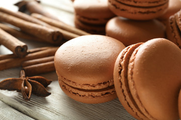 Tasty chocolate macarons and cinnamon on wooden background