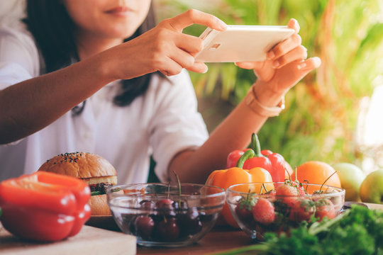 woman holding smart phone take a photo of food on table.
