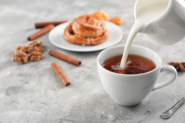 Adding milk to delicious tea on table