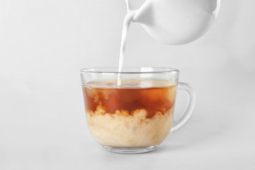 Adding milk to delicious tea on light background