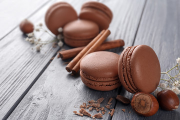 Delicious chocolate macarons and cinnamon sticks on wooden background