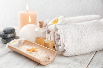 Fototapeta na wymiar Spa composition with sea salt, candles and rolled towels on light background