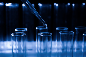 Pipette dripping sample into test tube on dark background, closeup