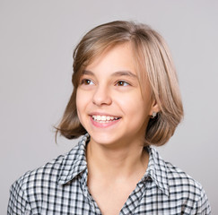 Beautiful caucasian teen girl on gray background. Schoolgirl smiling and looking away. Happy child - emotional portrait close-up.