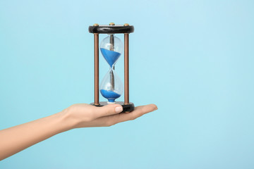 Woman holding hourglass on color background. Time management concept