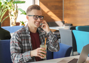 Young freelancer drinking cocktail while talking on mobile phone in cafe