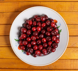 Ripe cherries with green leaves are on the plate.