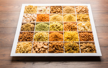 Indian Tea-time snacks like sev, chivda, farsan, mixture, boondi, bakarwadi etc served in white wooden box with cells. selective focus