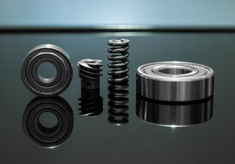 Close up view. Spare parts is spring with bearing and cog are small placed on black glass floor. There is reflection with background as backlight.