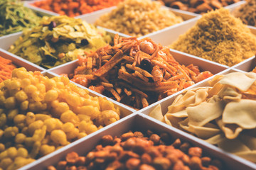 Indian Tea-time snacks like sev, chivda, farsan, mixture, boondi, bakarwadi etc served in white wooden box with cells. selective focus