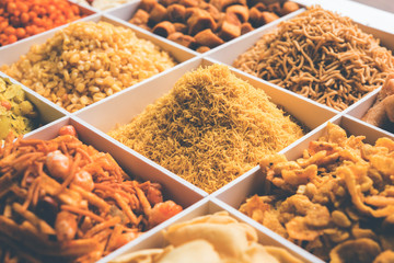 Indian Tea-time snacks like sev, chivda, farsan, mixture, boondi, bakarwadi etc served in white wooden box with cells. selective focus