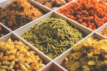 Indian Tea-time snacks like sev, chivda, farsan, mixture, boondi, bakarwadi etc served in white wooden box with cells. selective focus