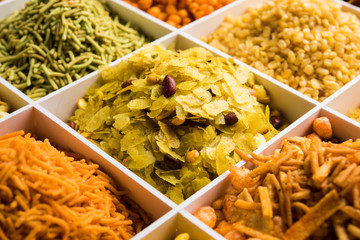 Indian Tea-time snacks like sev, chivda, farsan, mixture, boondi, bakarwadi etc served in white wooden box with cells. selective focus