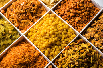 Indian Tea-time snacks like sev, chivda, farsan, mixture, boondi, bakarwadi etc served in white wooden box with cells. selective focus