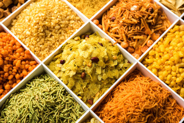 Indian Tea-time snacks like sev, chivda, farsan, mixture, boondi, bakarwadi etc served in white wooden box with cells. selective focus