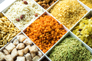 Indian Tea-time snacks like sev, chivda, farsan, mixture, boondi, bakarwadi etc served in white wooden box with cells. selective focus