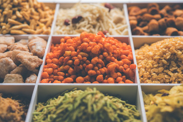 Indian Tea-time snacks like sev, chivda, farsan, mixture, boondi, bakarwadi etc served in white wooden box with cells. selective focus