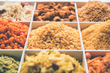Indian Tea-time snacks like sev, chivda, farsan, mixture, boondi, bakarwadi etc served in white wooden box with cells. selective focus