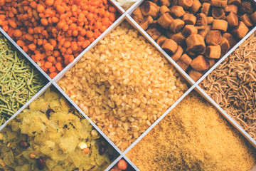 Indian Tea-time snacks like sev, chivda, farsan, mixture, boondi, bakarwadi etc served in white wooden box with cells. selective focus