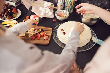 Cropped image of siblings decorating cake at kitchen counter