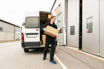 Manual worker carrying cardboard box while walking against delivery van on road