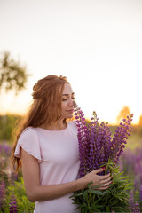 beautiful sexy woman in white sundress with a bouquet in the hands of lupine in field