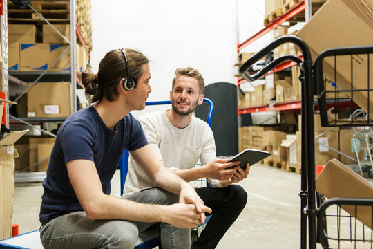 Male colleagues discussing over digital tablet while sitting on push cart at industry