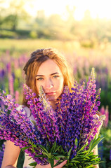beautiful sexy woman in white sundress with a bouquet in the hands of lupine in field close-up