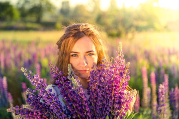 beautiful sexy woman in white sundress with a bouquet in the hands of lupine in field close-up
