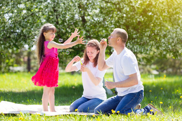 Little girl is playing with soap bubbles. Parents let the soap bubbles on their daughter in the summer in the park.