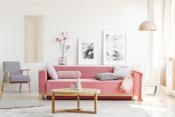 Patterned armchair and pink couch in feminist apartment interior with flowers and posters. Real...